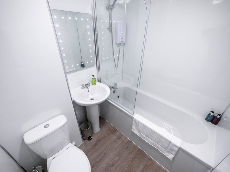 Modern bathroom with toilet, pedestal sink, bathtub, glass shower enclosure and mirror