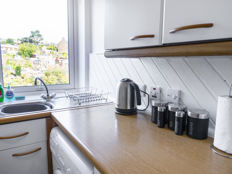 Modern kitchen with white cabinetry, wooden countertop, kettle and storage containers, window view