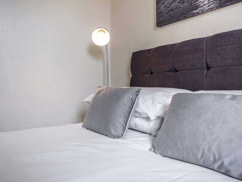 Modern bedroom with grey upholstered headboard, white bedding, grey pillows and floor lamp