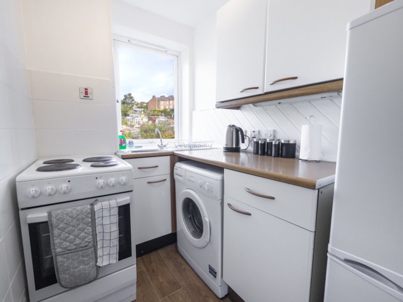 Compact kitchen with white units, electric cooker, washing machine and window view