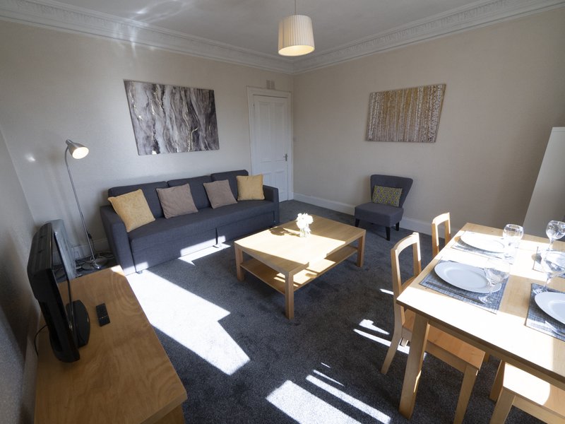 Open-plan living and dining area with sofa, coffee table, and dining set with place settings