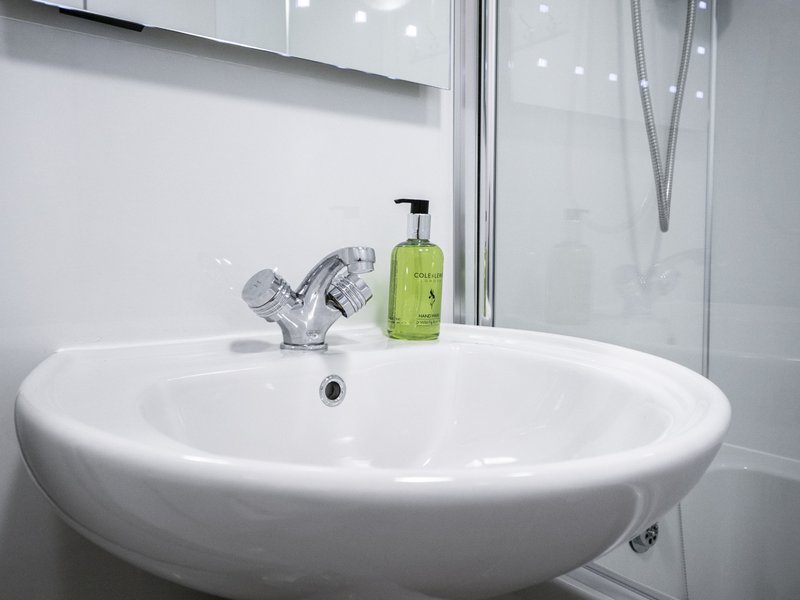 Modern white round bathroom sink with chrome tap and green soap dispenser
