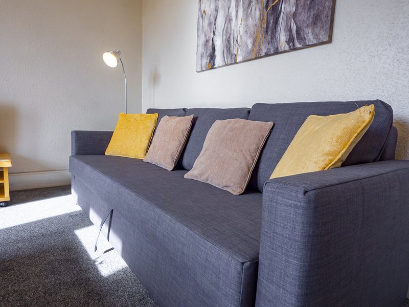 Modern living room with gray sofa, yellow and beige cushions, floor lamp and wall art