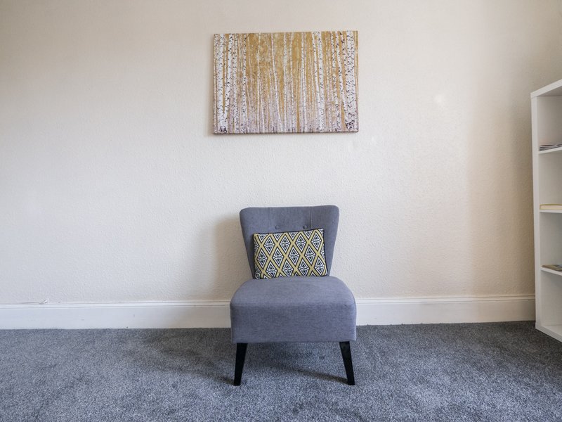 Modern bedroom with grey upholstered chair, geometric cushion, and abstract wall art