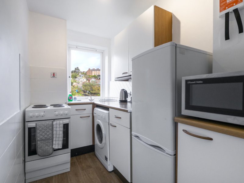 Compact kitchen with white appliances, microwave, window view and wooden flooring