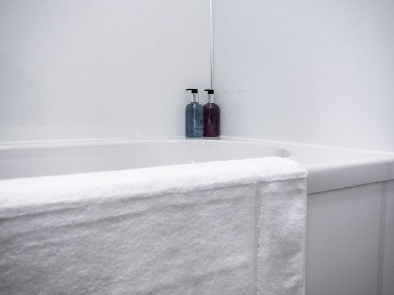 Modern bathroom with white bathtub, marble surround, and toiletry bottles on shelf