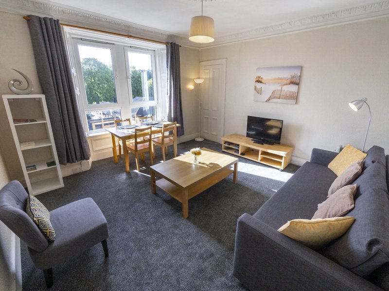Spacious living room with gray sofa, wooden coffee table, dining area and patio doors
