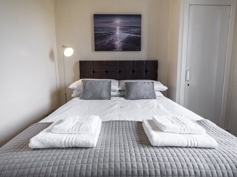 Modern bedroom with double bed, grey headboard, white bedding, and framed seascape artwork