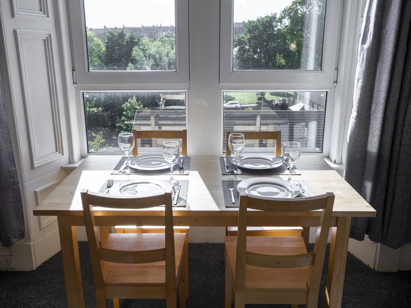 Dining table set for two with wooden chairs, large windows overlooking garden views