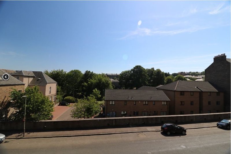 Elevated view of residential street with brick buildings, parked cars, and tree-lined background