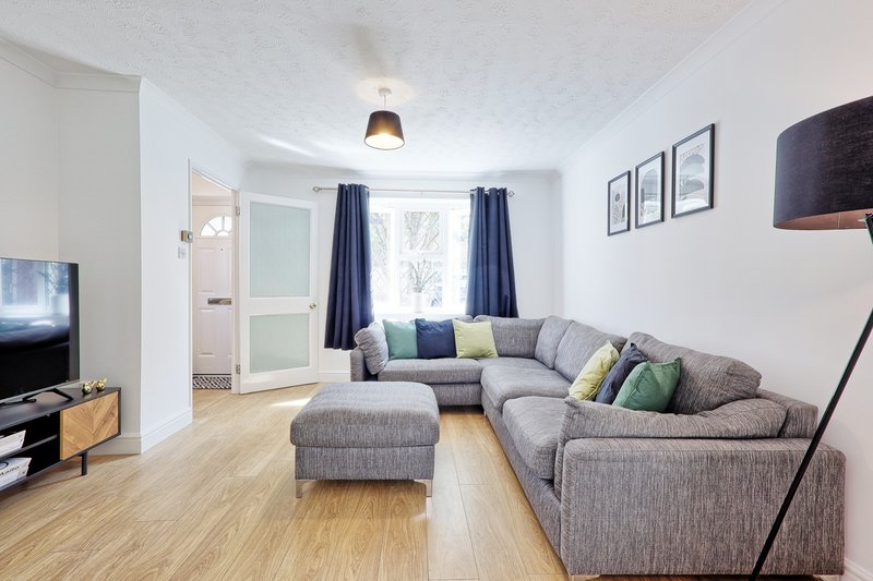 Bright living room with grey L-shaped sofa, wooden floor, TV, and blue curtains