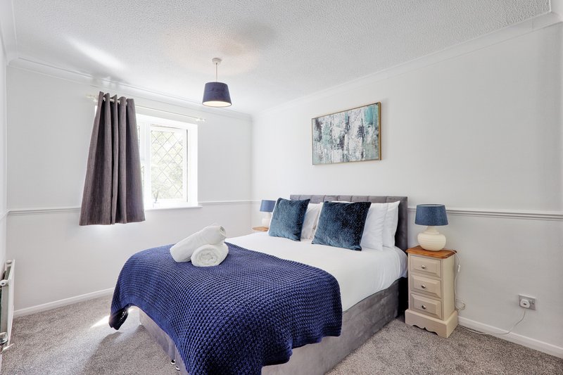 Modern bedroom with double bed, blue bedding, white pillows, wooden nightstand and pendant lamp