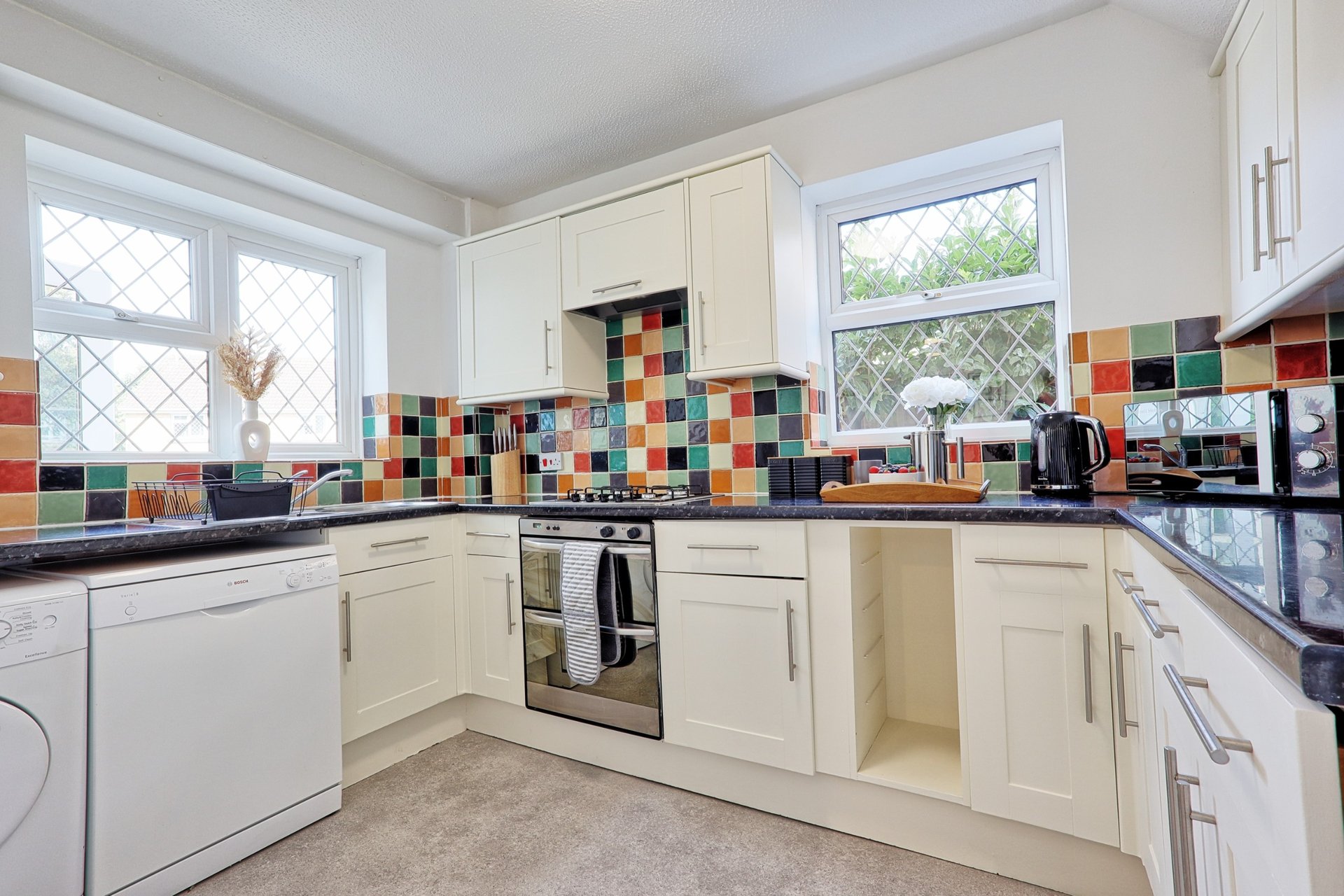 Cream kitchen with colorful tile backsplash, stainless steel oven, and windows overlooking garden
