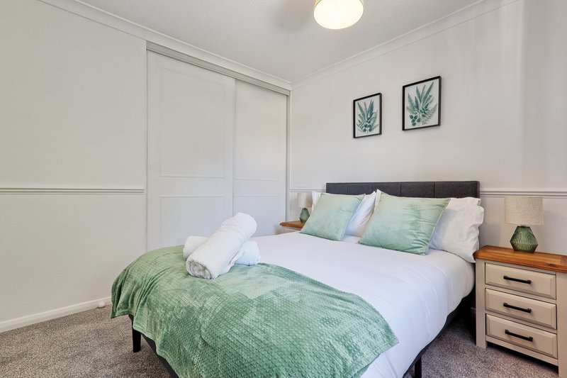 Bedroom with double bed, green bedding, white pillows, wooden nightstand and sliding wardrobe