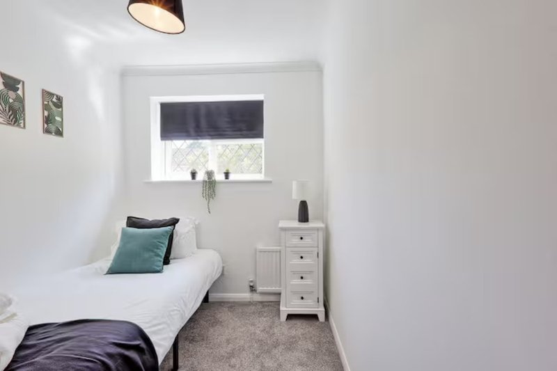 Small bedroom with single bed, white bedside table, window with blind, and pendant light