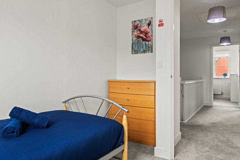 Bedroom with blue bedding, wooden dresser, framed floral artwork, and open doorway to hallway