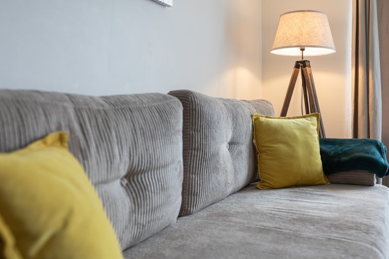Modern bedroom with grey upholstered bed, yellow and teal cushions, tripod floor lamp