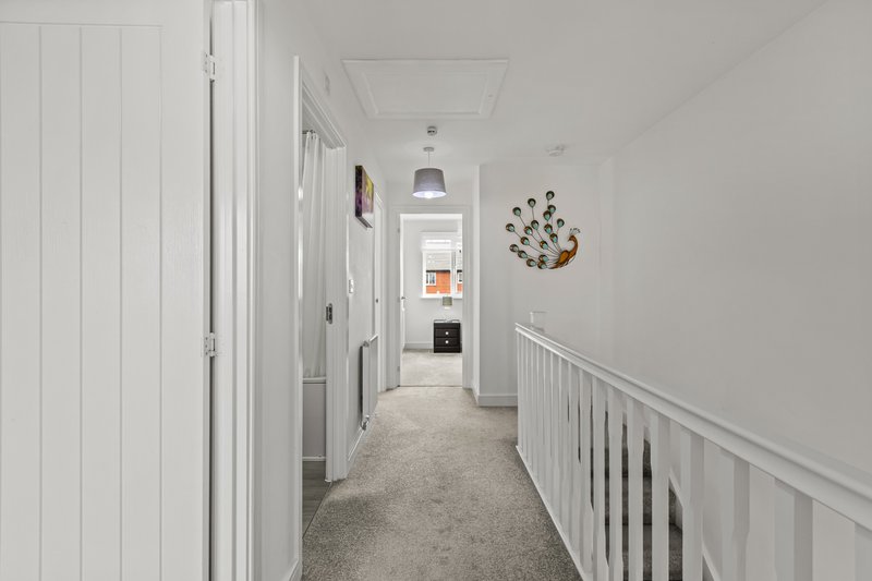 Long hallway with white walls, carpet flooring, white railing and decorative wall clock