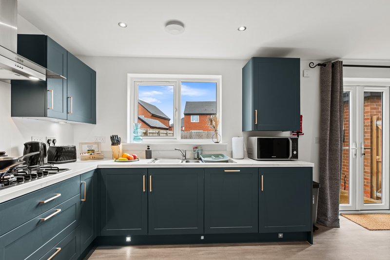 Modern kitchen with dark teal cabinetry, white countertops, gas hob and window overlooking residential street