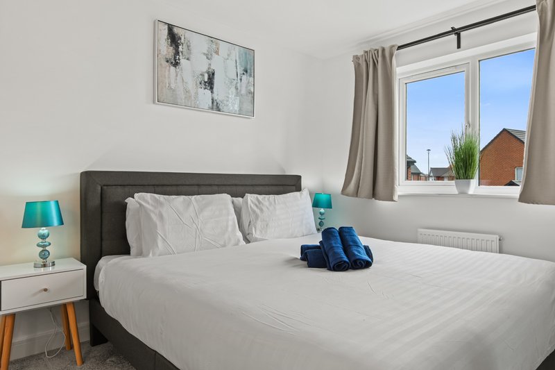 Modern bedroom with double bed, grey headboard, white bedding, and bright window overlooking garden