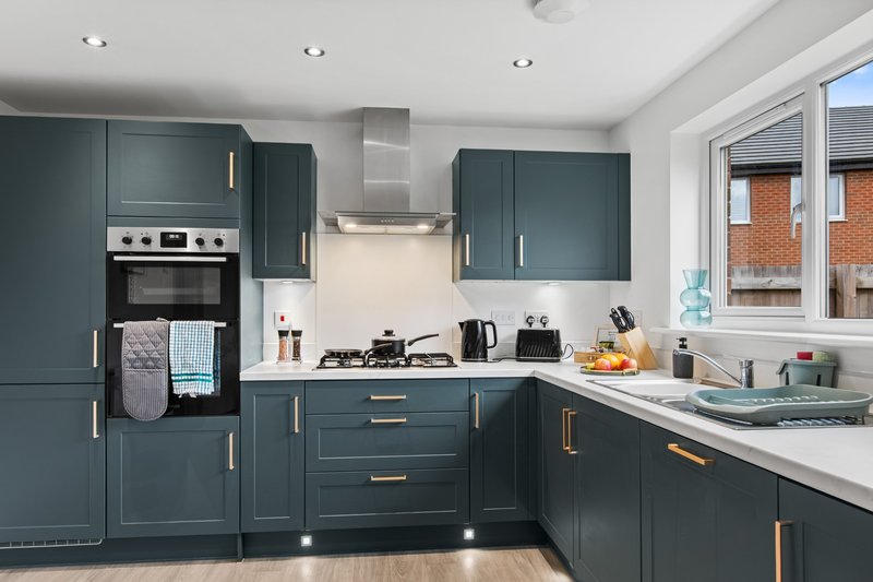 Modern kitchen with dark teal cabinetry, stainless steel appliances, white countertop and brick exterior visible through windows