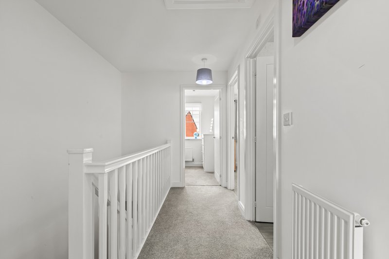 Bright upstairs hallway with white railings, grey carpet and multiple doors