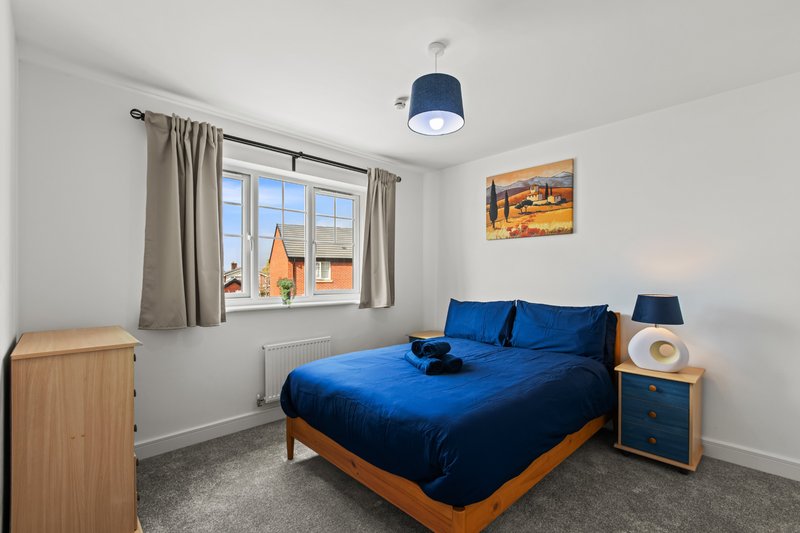 Bright bedroom with blue bedding, wooden bed frame, pendant lamp, and window with garden views