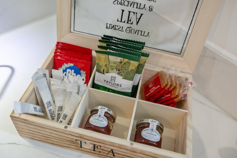 Wooden tea organizer box with compartments containing tea bags, jars, and packets