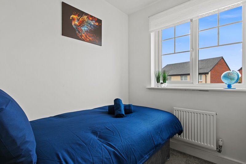 Bedroom with blue double bed, wall art, large window overlooking houses and garden