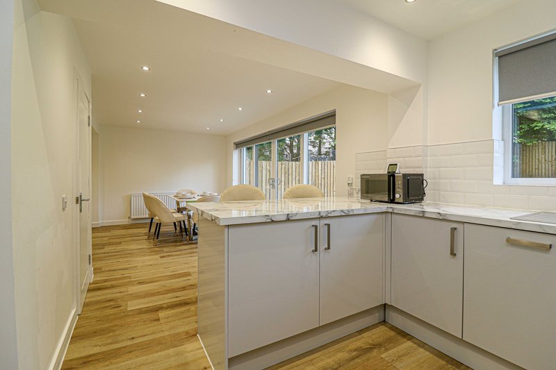Modern kitchen with white cabinets, wooden flooring, and open-plan dining area beyond
