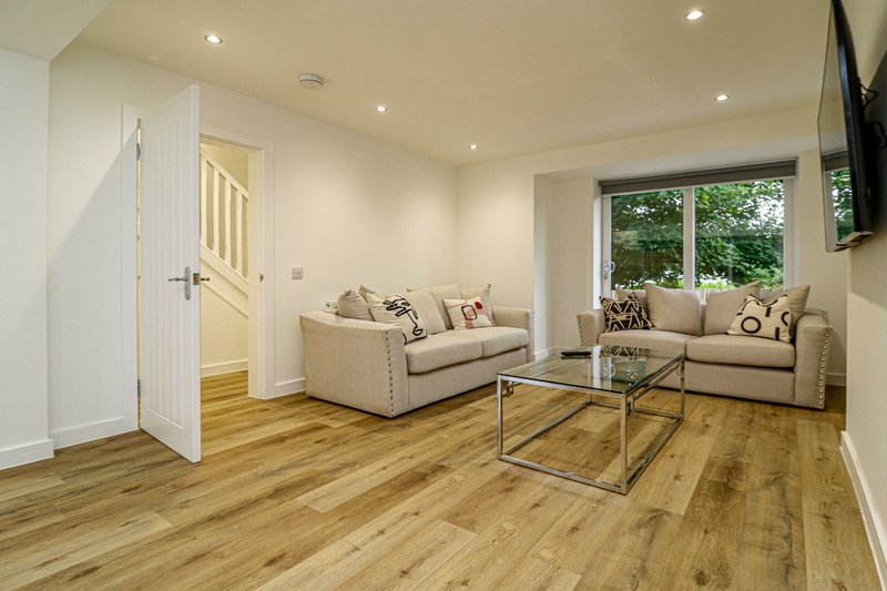 Spacious living room with two beige sofas, wooden flooring, glass coffee table and garden view