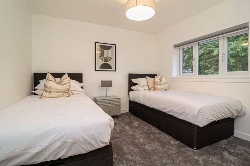 Twin bedroom with two black beds, white bedding, decorative pillows, and large windows