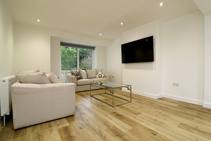 Modern living room with cream sofa, wall-mounted TV, wooden flooring and garden view