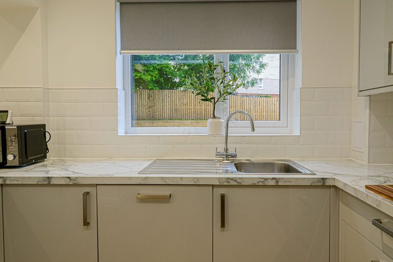 Modern kitchen with cream cabinetry, marble countertop, stainless steel sink and window view of garden