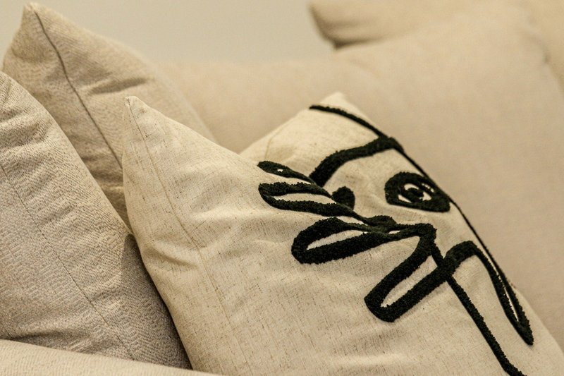 Close-up of cream cushion with black abstract face embroidery design