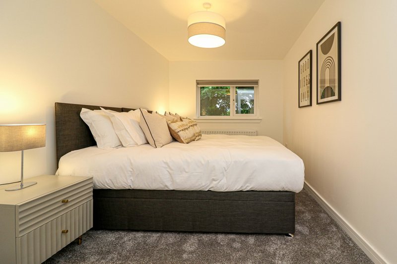 Compact bedroom with double bed, dark headboard, bedside lamp and window