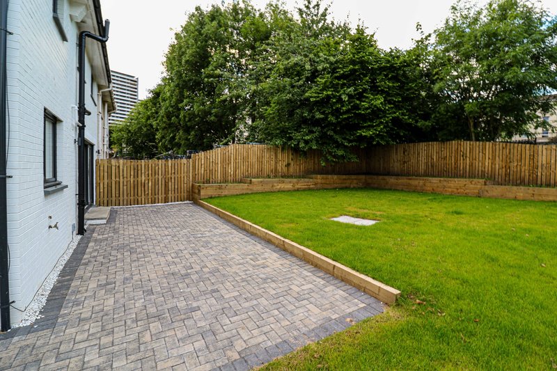 Modern house exterior with paved patio, green lawn, wooden fence and landscaping