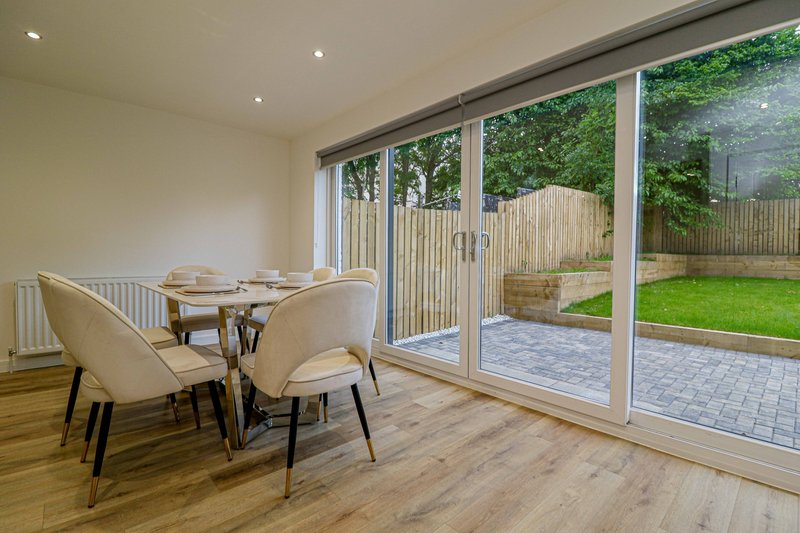 Modern dining area with wooden table, cream chairs, and large sliding doors opening to garden patio