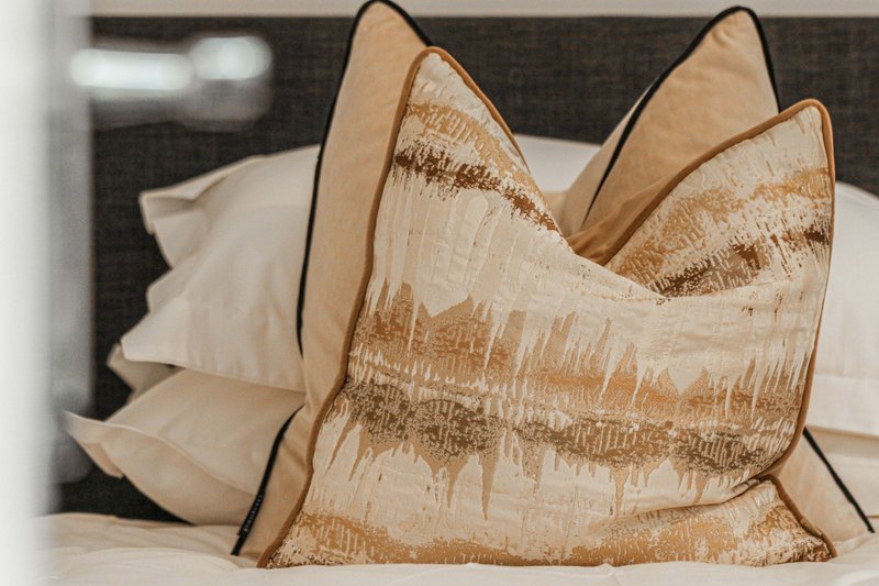 Decorative cushions with gold and cream patterned fabric on bed with white bedding