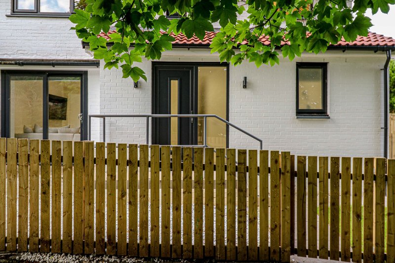 White brick cottage exterior with wooden fence, entrance door and windows