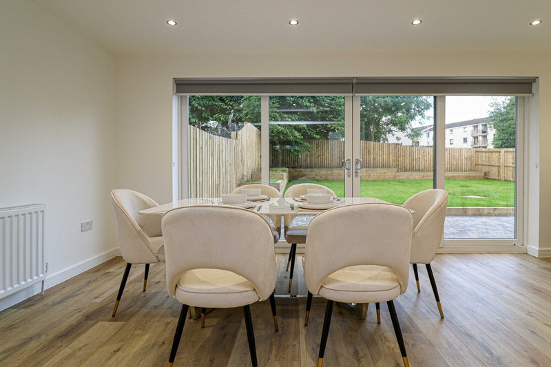 Modern dining area with round glass table, beige chairs, and sliding doors opening to garden