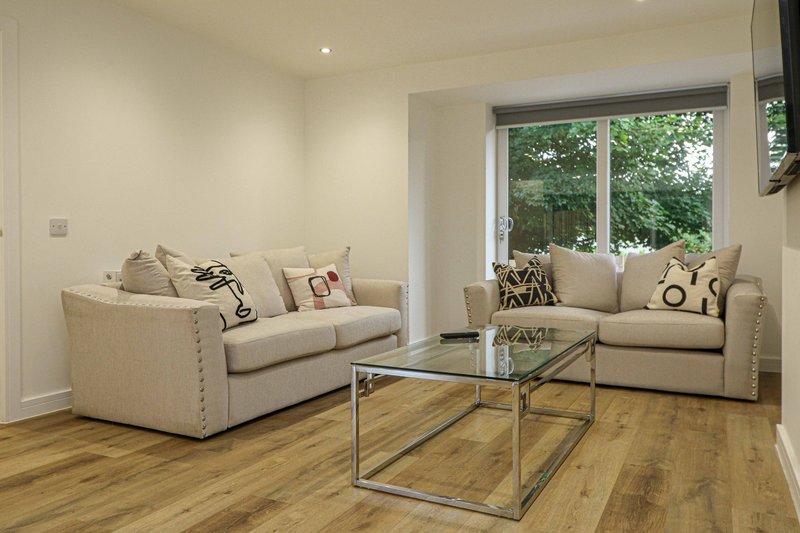 Bright living room with cream sofas, glass coffee table, wooden floor and garden views