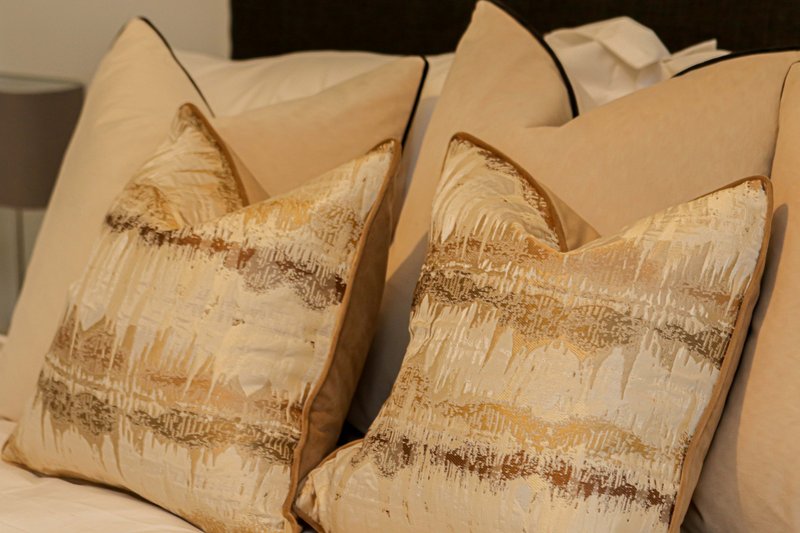 Bed with decorative gold and cream patterned cushions and white headboard