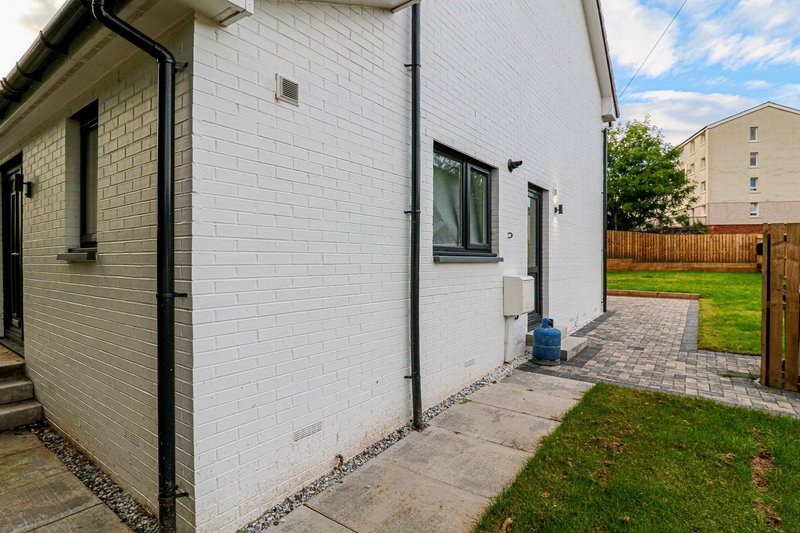 Modern white-brick house exterior with patio, garden, wooden fence and neighboring buildings