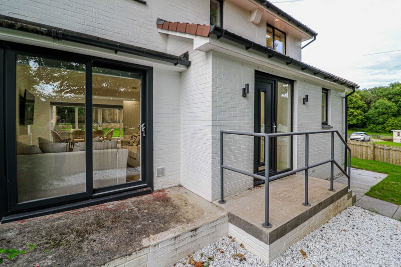 Modern white brick house exterior with black-framed glass doors, metal railing, and paved patio area