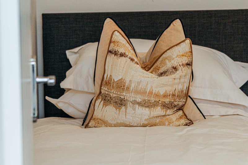 Bedroom with upholstered headboard, white pillows, and gold decorative cushion on bed