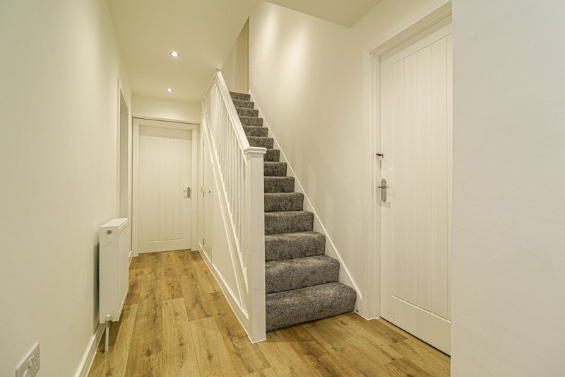 Bright hallway with wooden flooring, white walls, staircase with grey carpet and white bannister