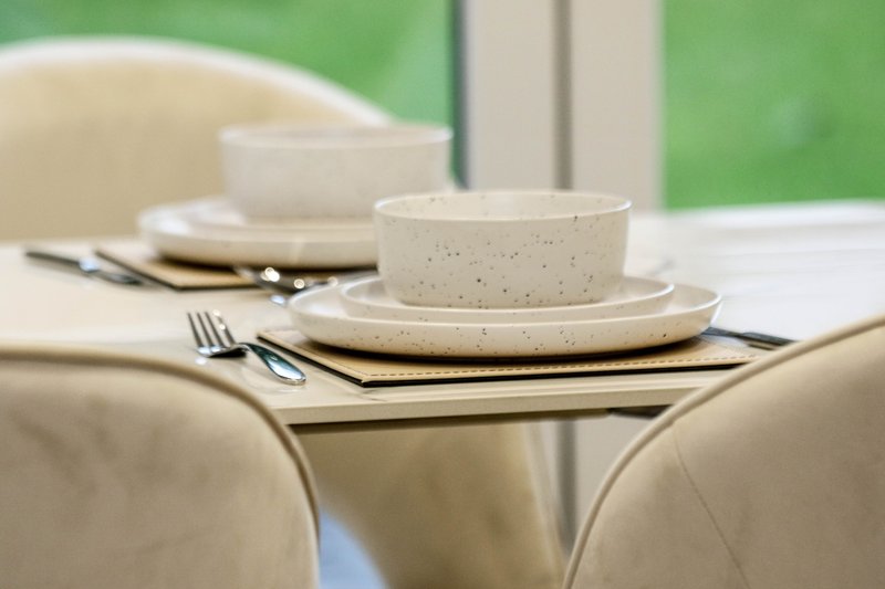 Dining table set with cream ceramic dishware, cutlery, and napkins