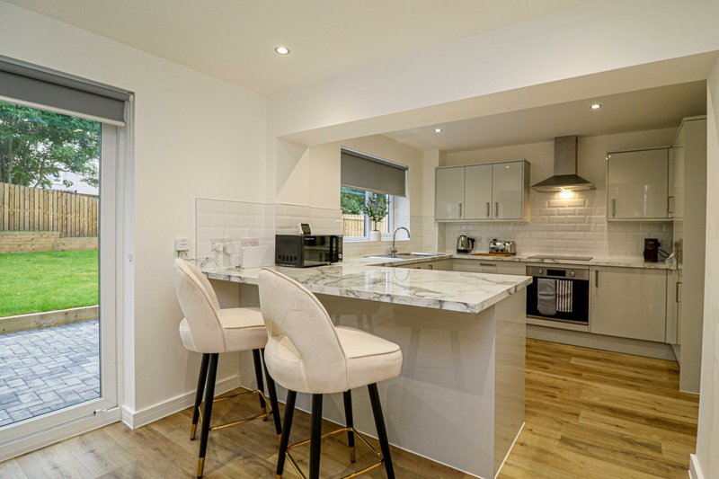 Modern kitchen with island, two bar stools, cream cabinetry, and garden view through patio doors