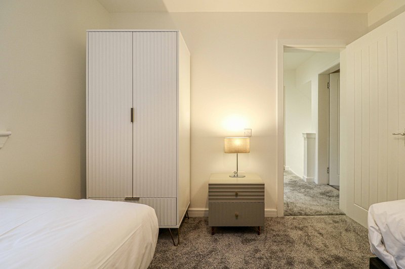 Bedroom with two single beds, wardrobe, bedside table with lamp, and corridor to ensuite
